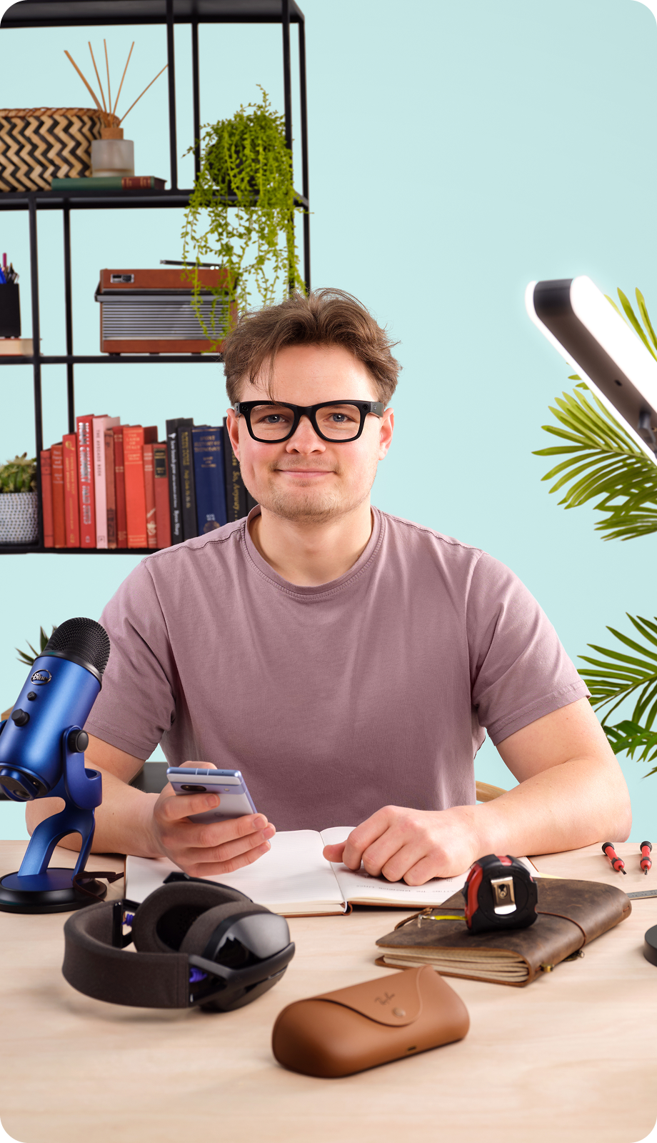 Phil Make Stuff sat behind a wooden desk with a microphone, notebooks, smart glasses and a gaming headset