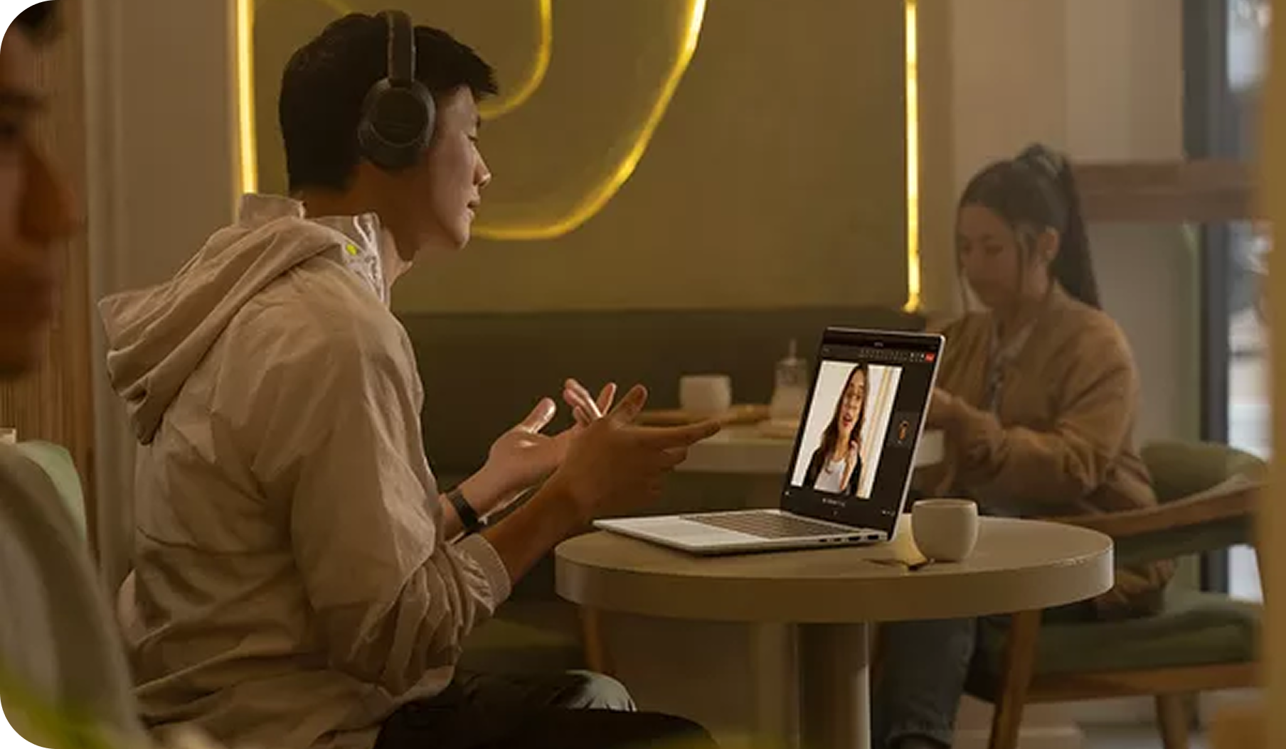 A man making a video call in a coffee shop. A women in the background